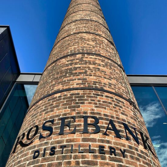 Der historische Ziegel-Schornstein der Rosebank Distillery ragt in den blauen Himmel Schottlands.