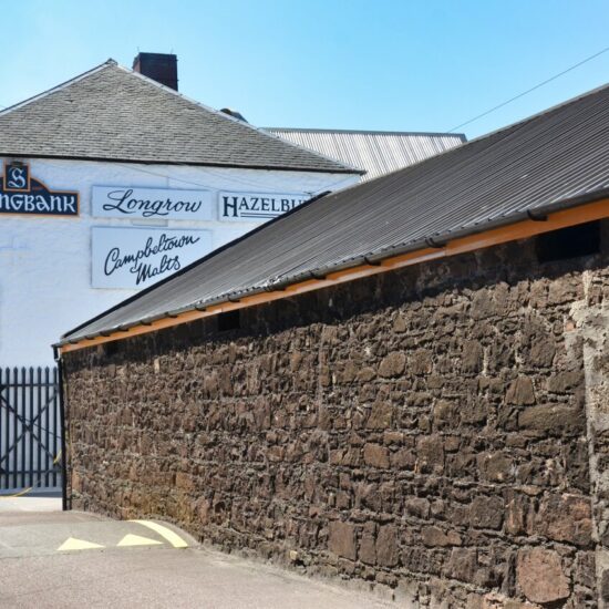 Campbeltown: Zwischen dem Ende der Bruchsteinfassade vom Springbank Whisky-Warehouse und dem weißen Verwaltungsgebäude liegt das Eingangstor zu Destillerie.